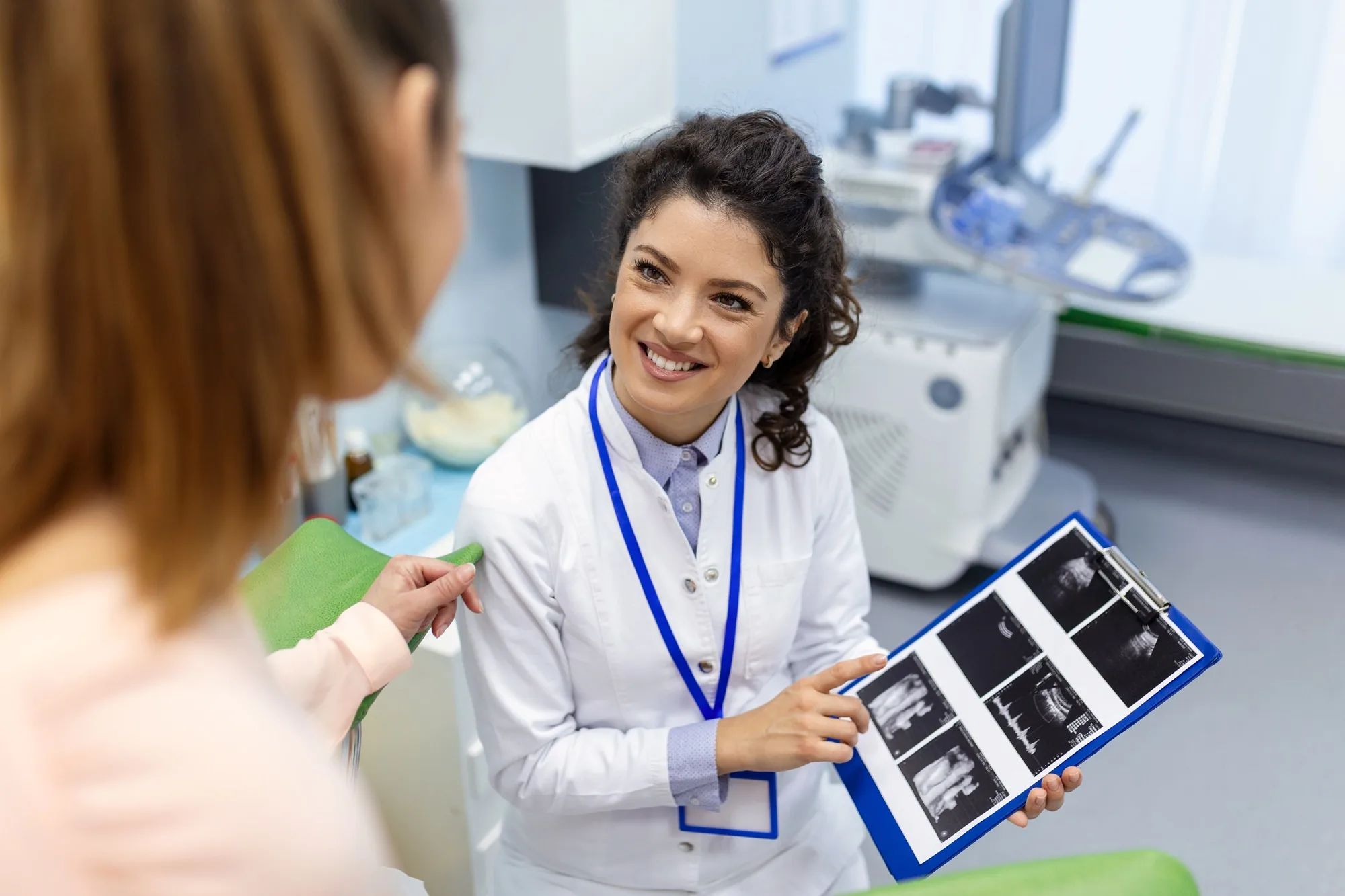 Female doctor smiling while showing ultrasound scans on a clipboard to a patient
